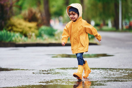 Kid in yellow waterproof cloak and boots playing outdoors after the rain