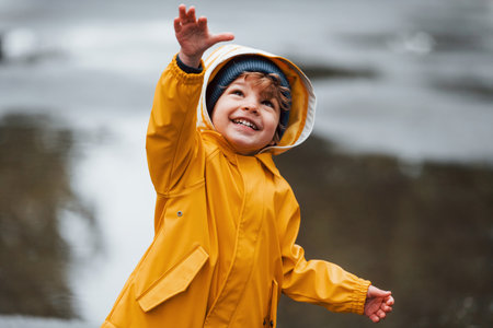 Kid in yellow waterproof cloak and boots playing outdoors after the rainの写真素材