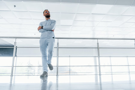 Leaning on silver colored railings. Young handsome man in formal clothes indoors in the office at daytimeの写真素材