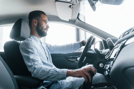 Side view of young handsome man in formal clothes that sitting in brand new automobileの写真素材