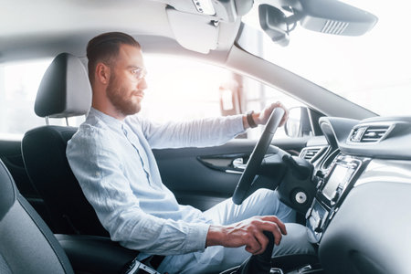 Side view of young handsome man in formal clothes that sitting in brand new automobile