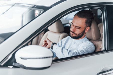 Side view of young handsome man in formal clothes that sitting in brand new automobile