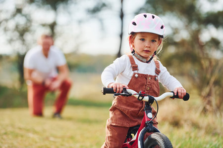 Father in white shirt teaching daughter how to ride bicycle outdoorsの写真素材