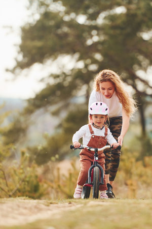 Mother in white shirt teaching daughter how to ride bicycle outdoorsの写真素材