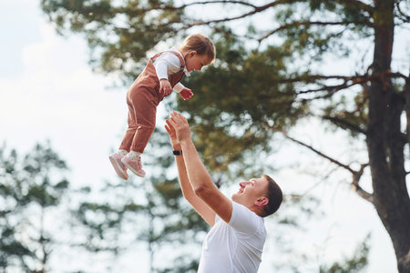 Father in casual clothes have walk and fun with daughter outdoors near forestの写真素材