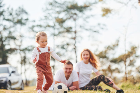 Playing with soccer ball. Father and mother spending weekend outdoors near forest with daughterの写真素材
