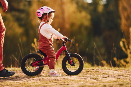 Beautiful sunlight. Father in white shirt teaching daughter how to ride bicycle outdoorsの写真素材