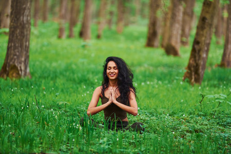 Positive brunette in casual clothes meditating in the forest at daytimeの写真素材