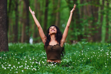 Positive brunette in casual clothes sitting in the forest at daytimeの写真素材