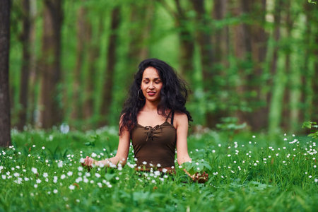 Positive brunette in casual clothes meditating in the forest at daytimeの写真素材