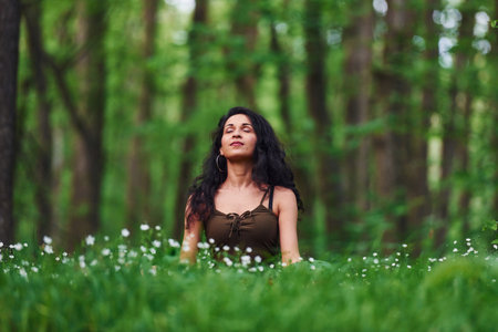 Positive brunette in casual clothes meditating in the forest at daytimeの写真素材