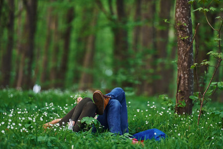 Couple lying down on the grass in forest together at daytimeの写真素材