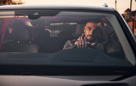 Front view of handsome unshaved man in fashionable clothes that riding his automobileの写真素材