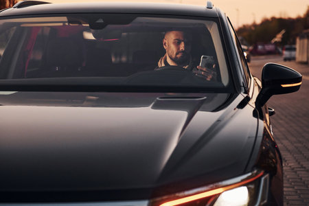 Front view of handsome unshaved man in fashionable clothes that riding his automobileの写真素材
