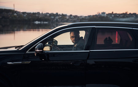 Side view of handsome unshaved man in fashionable clothes that riding his automobileの写真素材