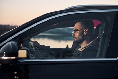 Side view of handsome unshaved man in fashionable clothes that riding his automobileの写真素材