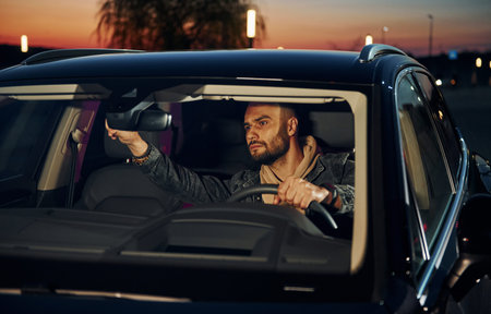 Handsome unshaved man in fashionable clothes riding his automobile