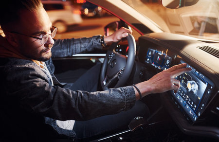 Using navigation display. Handsome unshaved man in fashionable clothes riding his automobile