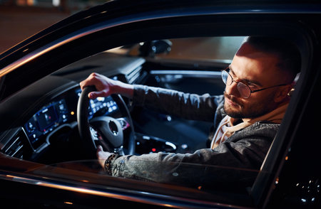 Side view of handsome unshaved man in fashionable clothes that riding his automobileの写真素材