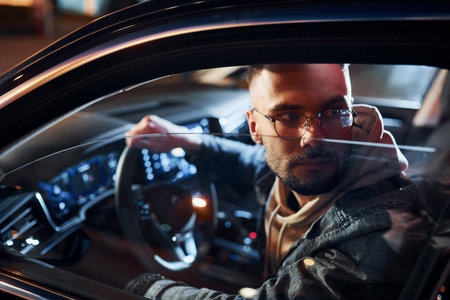 Side view of handsome unshaved man in fashionable clothes that riding his automobileの写真素材