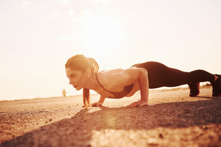 Woman in sportswear doing push-ups on the road at evening timeの写真素材