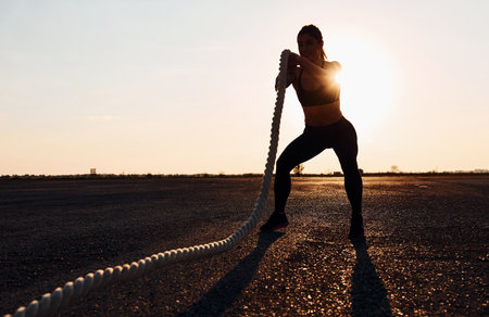 Woman in sportswear training with knots on the road at evening timeの写真素材