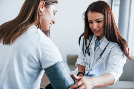 Measuring blood pressure. Young woman have a visit with female doctor in modern clinicの写真素材