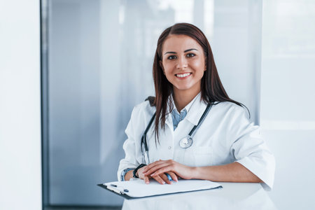 With notepad. Young nurse indoors in modern clinic. Conception of healthcareの写真素材