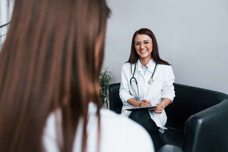 Sitting and talking. Young woman have a visit with female doctor in modern clinicの写真素材