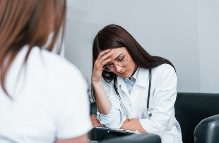 Sitting and talking. Young woman have a visit with female doctor in modern clinicの写真素材