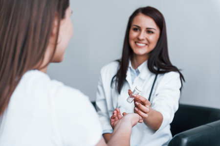 Doctor gives drugs to patient. Young woman have a visit with female doctor in modern clinicの写真素材