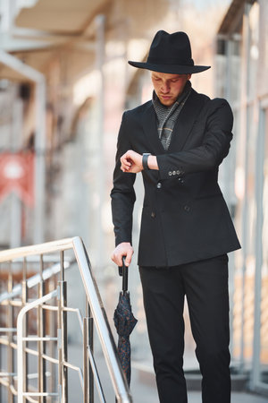 Elegant young man in black hat and with umbrella outdoors in the cityの写真素材