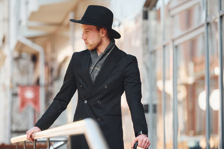 Elegant young man in black hat and with umbrella outdoors in the cityの写真素材