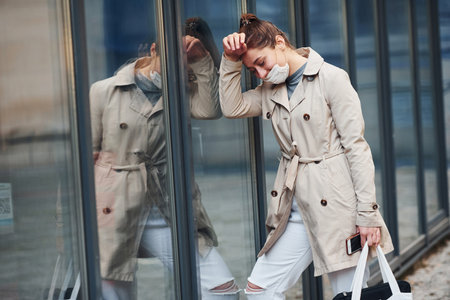 Young girl in coat and white protective mask standing outdoors near buildingの写真素材