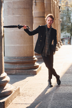 Holding umbrella. Elegant young man in formal classy clothes outdoors in the cityの写真素材