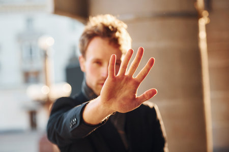 Shows stop gesture by the hand. Elegant young man in formal classy clothes outdoors in the cityの写真素材