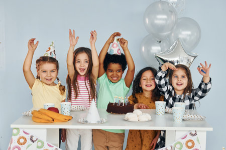 Sits by the table. Children on celebrating birthday party indoors have fun togetherの写真素材