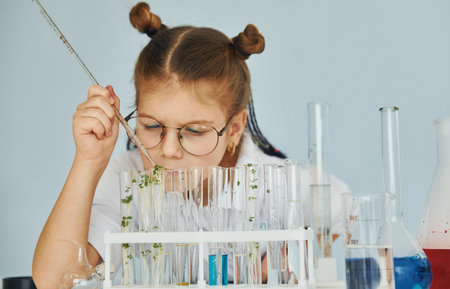 Workes with liquid that is in test tubes. Little girl in coat playing a scientist in lab by using equipmentの写真素材
