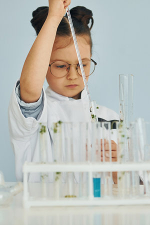 Workes with liquid that is in test tubes. Little girl in coat playing a scientist in lab by using equipmentの写真素材