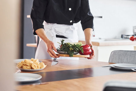 With vegetables. Professional young chef cook in uniform working on the kitchenの写真素材