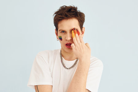Young gay man is standing in the studio and posing for a camera. Painted by multi colored makeupの写真素材