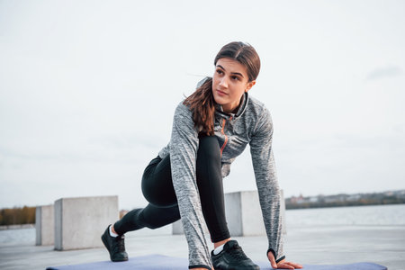 Young sportive girl doing yoga exercises on fitness mat outdoors near lake at daytimeの写真素材