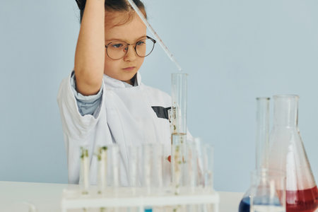 Workes with liquid that is in test tubes. Little girl in coat playing a scientist in lab by using equipmentの写真素材