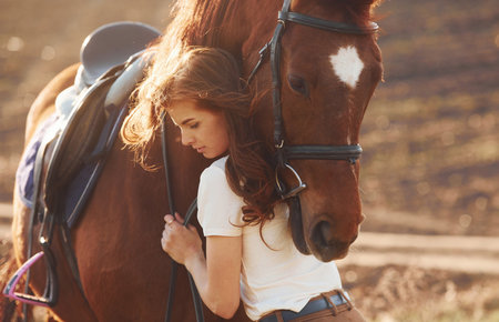Young woman embracing her horse in agriculture field at sunny daytimeの写真素材