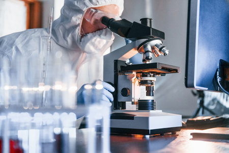 Monitors with information on the table. Scientist in white protective uniform works with coronavirus...