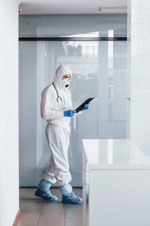 Male doctor scientist in lab coat, defensive eyewear and mask holding notepad in handsの写真素材