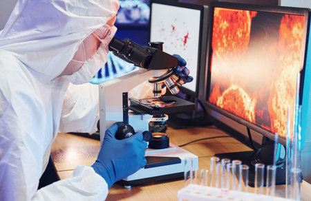 Scientist in white protective uniform near displays with data works with coronavirus and blood tubes...