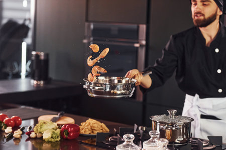 Professional young chef cook in uniform frying food on the kitchenの写真素材