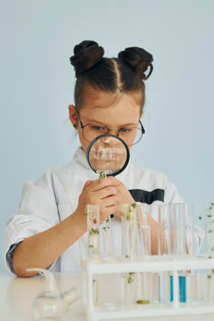 Workes with liquid that is in test tubes. Little girl in coat playing a scientist in lab by using equipmentの写真素材