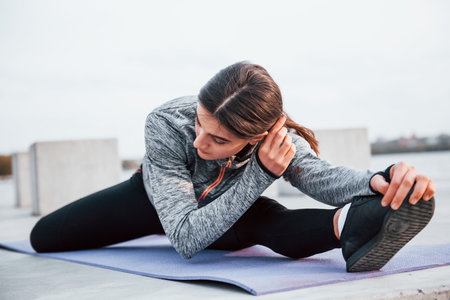Young sportive girl doing yoga exercises on fitness mat outdoors near lake at daytimeの写真素材
